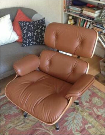 a walnut and tobacco leather reclining Eames chair, pictured in a living room in front of a bookcase and besides a sofa