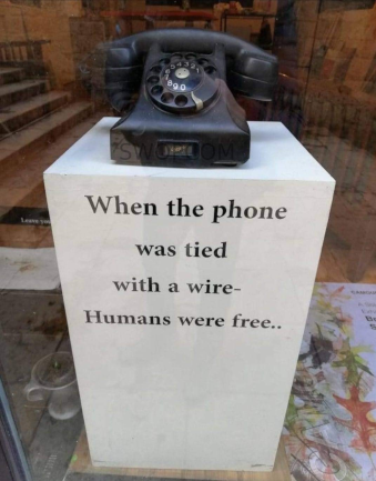 an old telephone sits on a plinth in an empty shop window. On the plinth are the words When the phone was tied with a wire - Humans were free